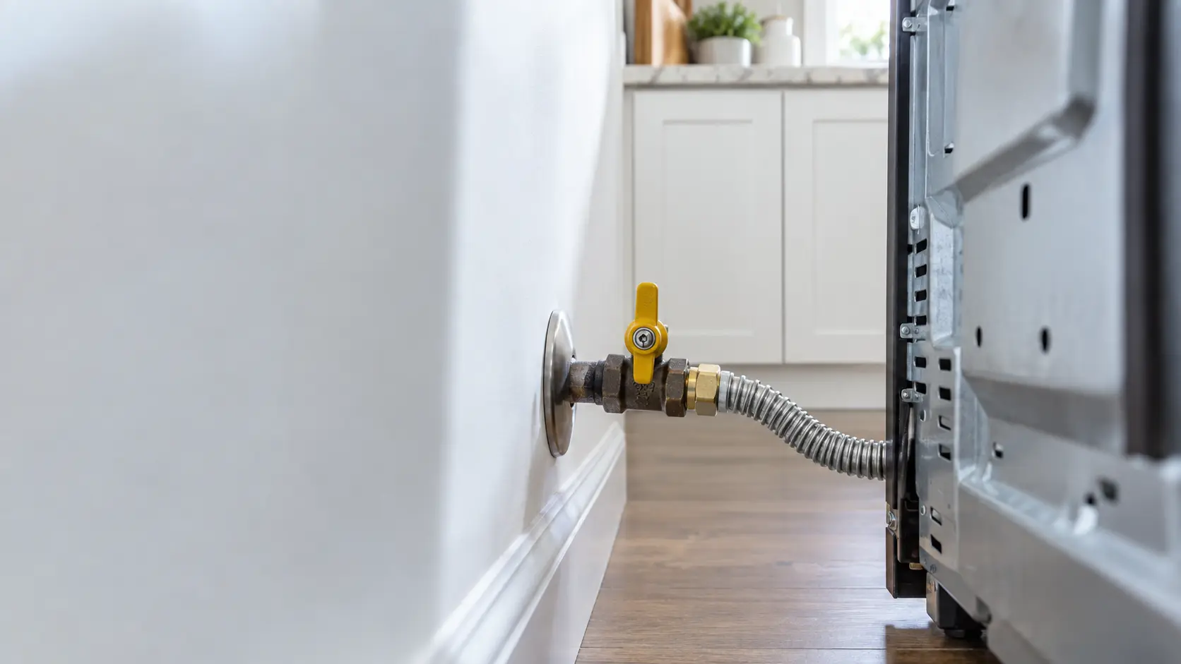 The closed gas shutoff valve behind a range, seen close.